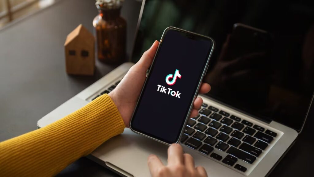 Personne tennant son smartphone sur l'application TikTok devant son ordinateur