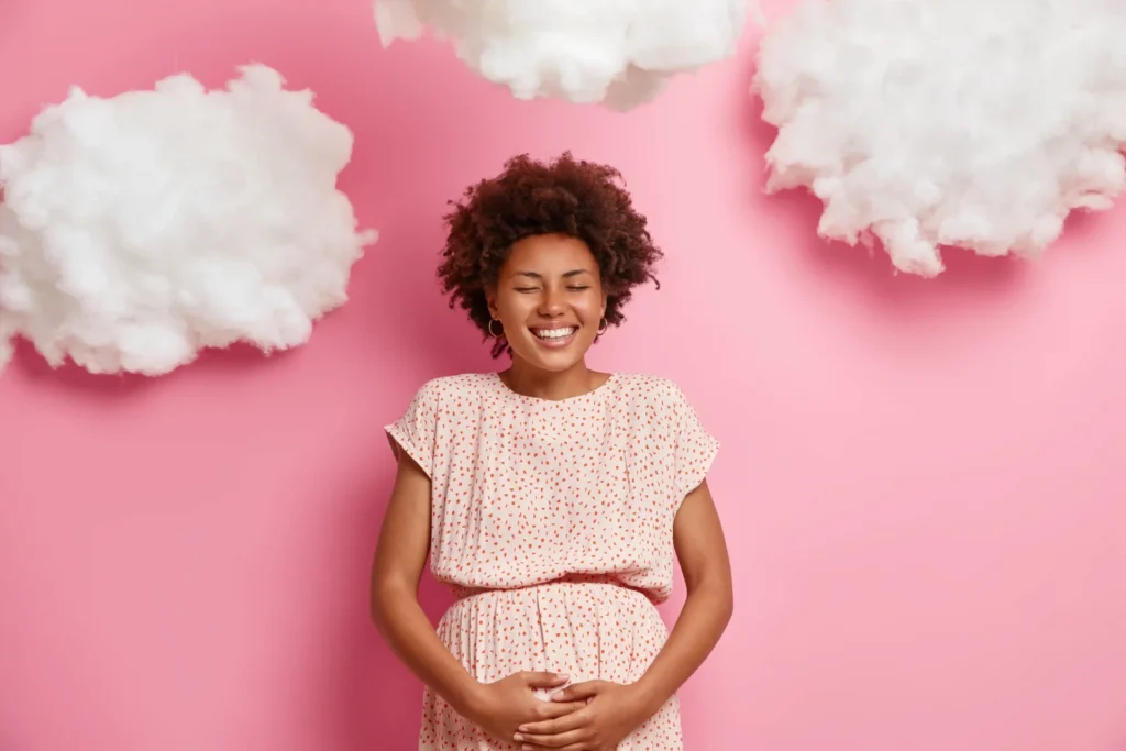 Femme enceinte devant un fond rose montrant qu'elle est enceinte